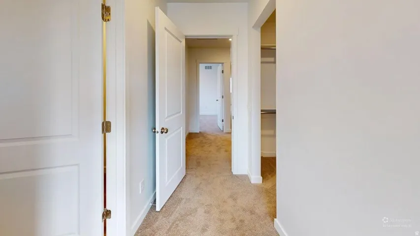 Carpeted hallway featuring white walls and white two-panel doors with brass hardware