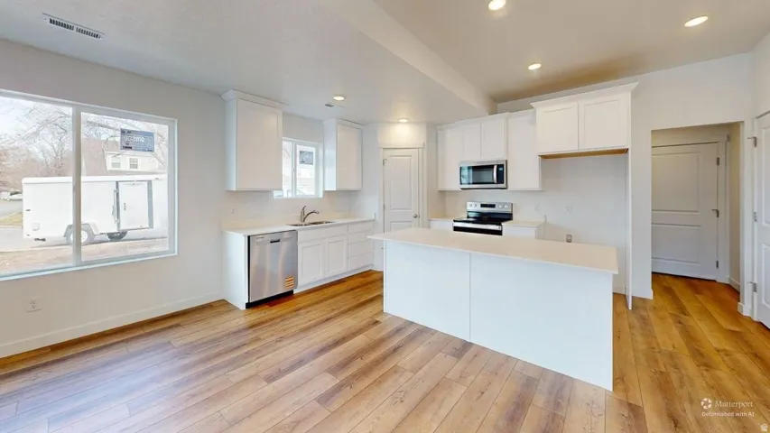 Modern kitchen featuring a central island, white cabinetry, stainless steel appliances, and wood-finish flooring