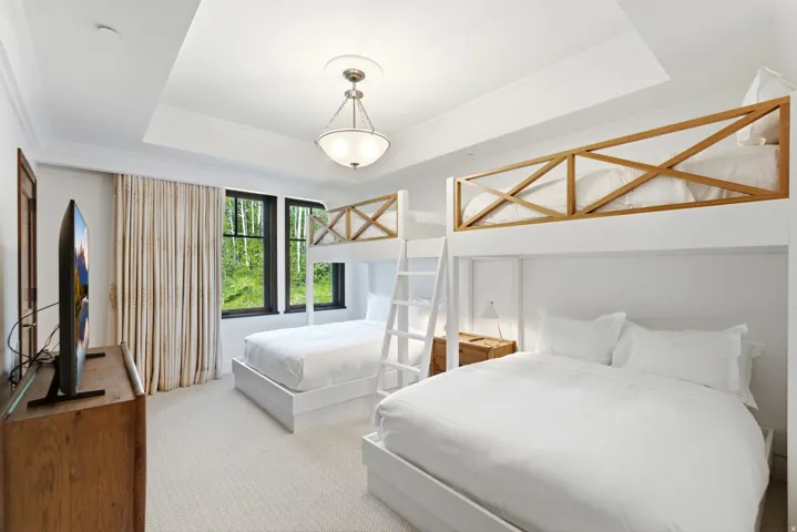 Room featuring bunk beds with natural wood railings, recessed ceiling with a central chandelier, and light-toned carpet flooring