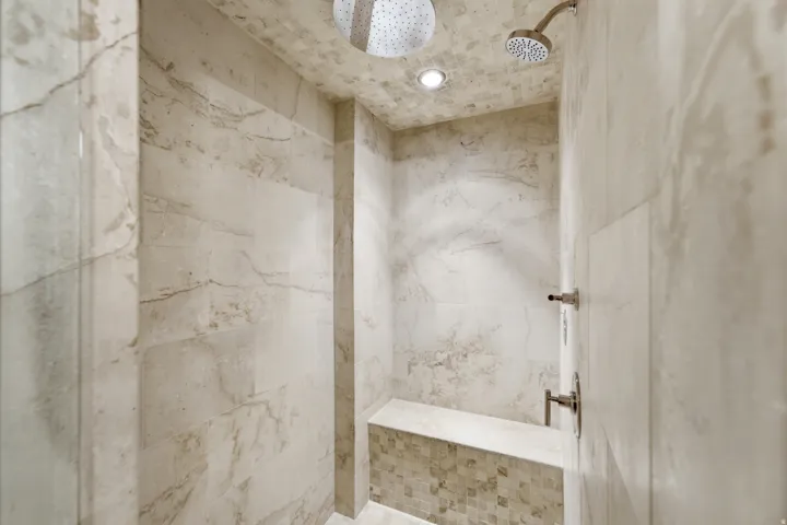 Spa-inspired shower featuring large format natural stone wall tiles, mosaic tile ceiling, dual shower heads including a rain shower fixture, and a built-in bench with mosaic tile detailing