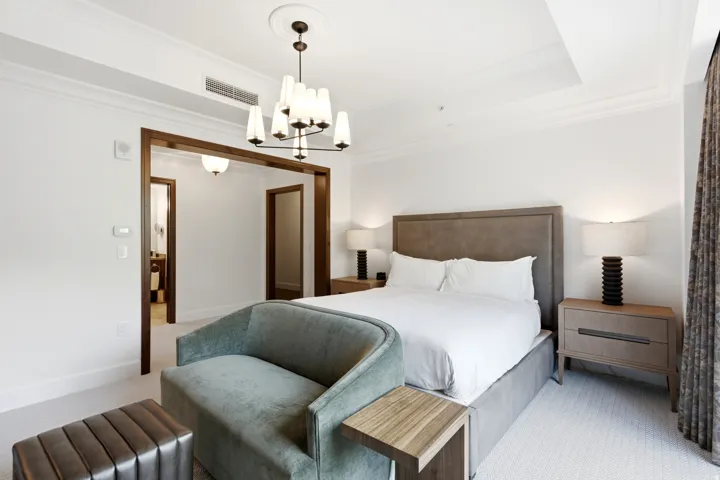 Spacious bedroom featuring a textured headboard, coordinating nightstands, a contemporary chandelier, crown molding, and a wide entryway