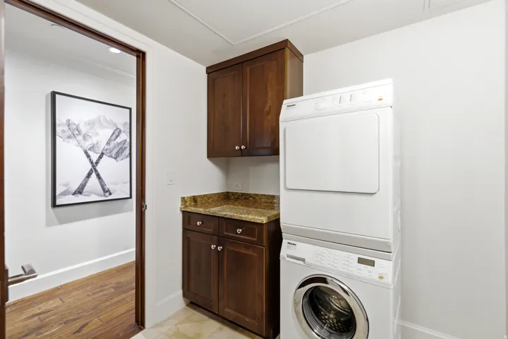 Laundry area featuring stacked appliances, dark wood cabinetry, and a speckled countertop
