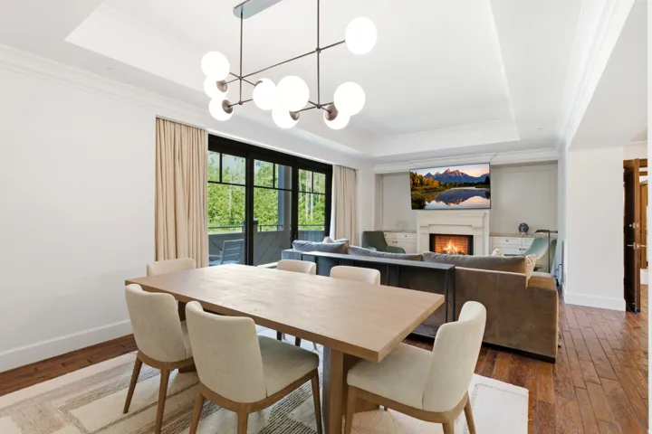 Open-concept living space featuring high ceilings with crown molding, a modern linear chandelier, and dark-framed glass doors