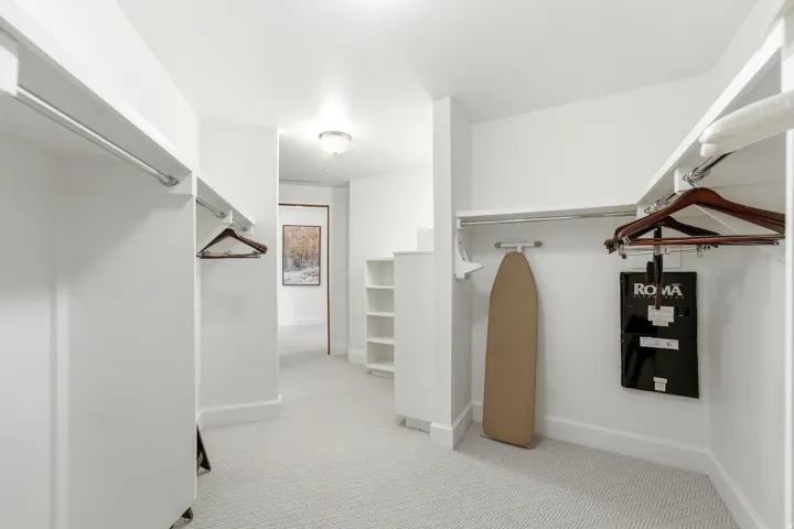 Walk-in closet with white shelving, hanging rods, and light-toned patterned carpeting