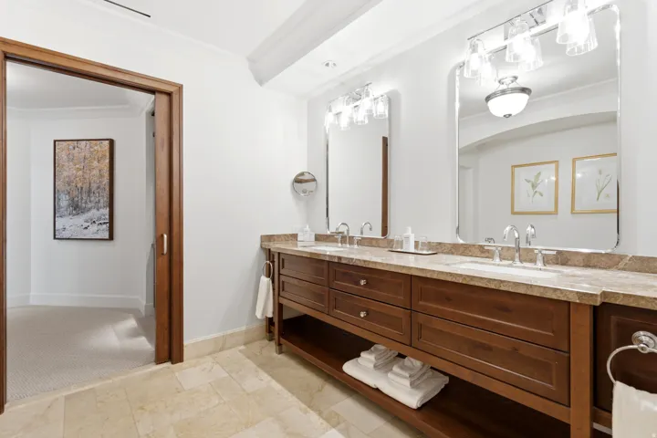Dual vanity featuring a stone countertop, individual sinks with chrome faucets, and custom wood cabinetry with integrated storage