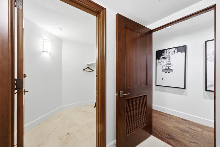 Entryway featuring a dark wood door with louvered panel, contrasting white baseboards, and wood-finish flooring