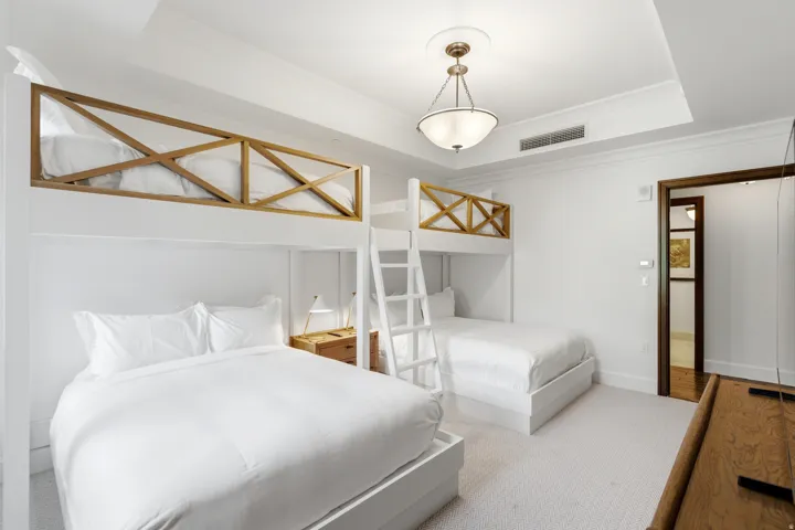Bedroom featuring built-in bunk beds with wooden safety rails, white bed frames, and light-toned carpeting