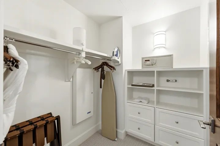 Walk-in closet featuring white built-in shelving, multiple drawers with silver hardware, a wall-mounted light fixture, and a security safe