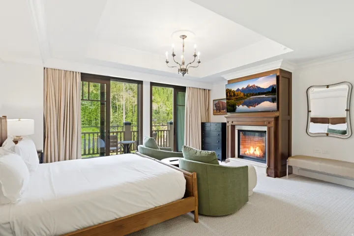 Room featuring a wood-surround fireplace, tray ceiling with chandelier, and two sets of glass-paneled doors opening to a balcony