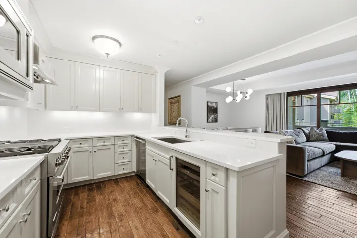 Modern kitchen featuring wood-finish flooring, white cabinetry, integrated range hood, stainless steel appliances, and a built-in beverage cooler
