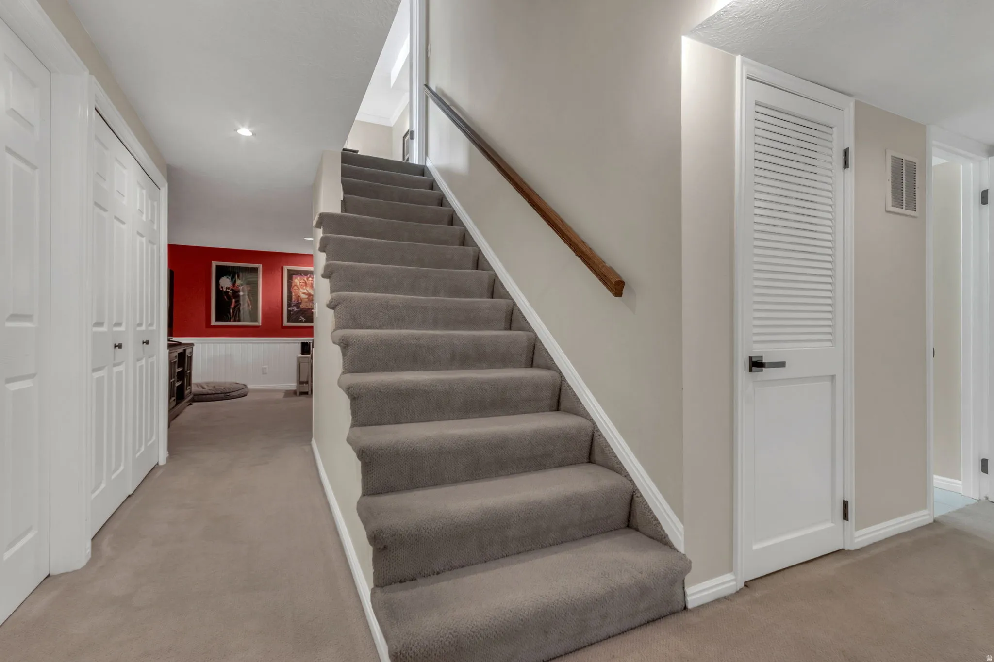 Basement staircase with carpeted treads and a wood handrail