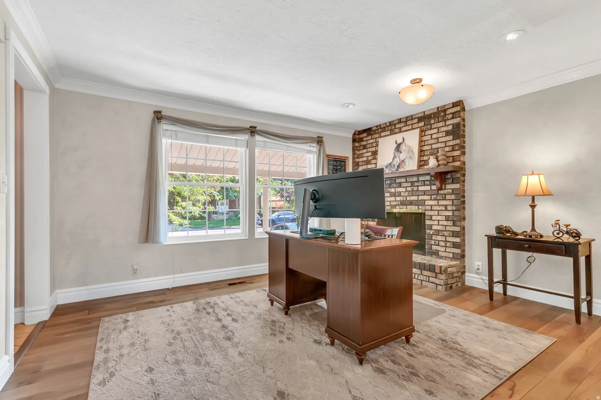Spacious room featuring wood-finish flooring, a brick fireplace, and crown molding