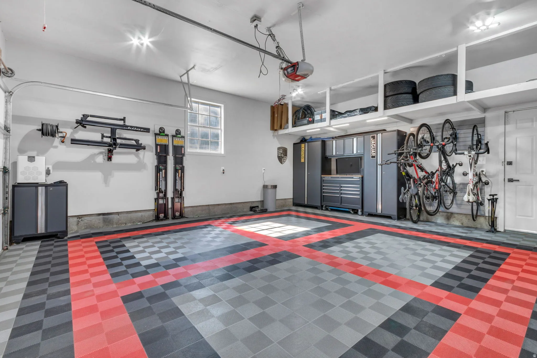Two-car garage featuring a patterned tile floor, built-in overhead storage shelves, wall-mounted storage solutions, recessed lighting, and a window for natural light