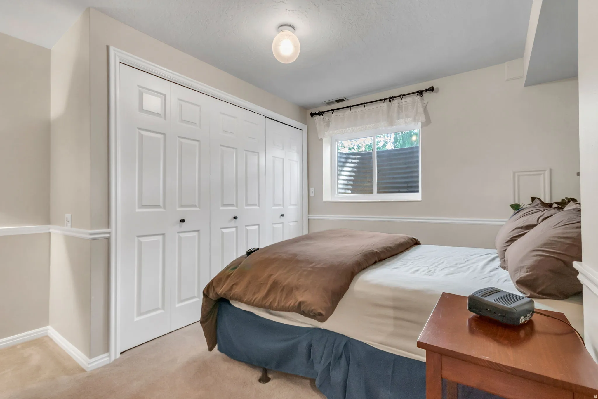 Bedroom 4:  featuring neutral carpeting, a large window, and a full-wall closet with bi-fold doors