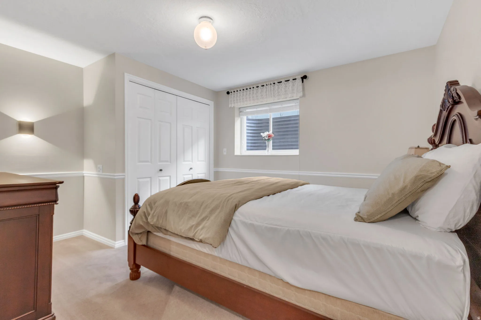 Bedroom 5: Neutral-toned room featuring a window with a valance, white bi-fold closet doors, wall sconce lighting, a ceiling-mounted light fixture, and carpet flooring