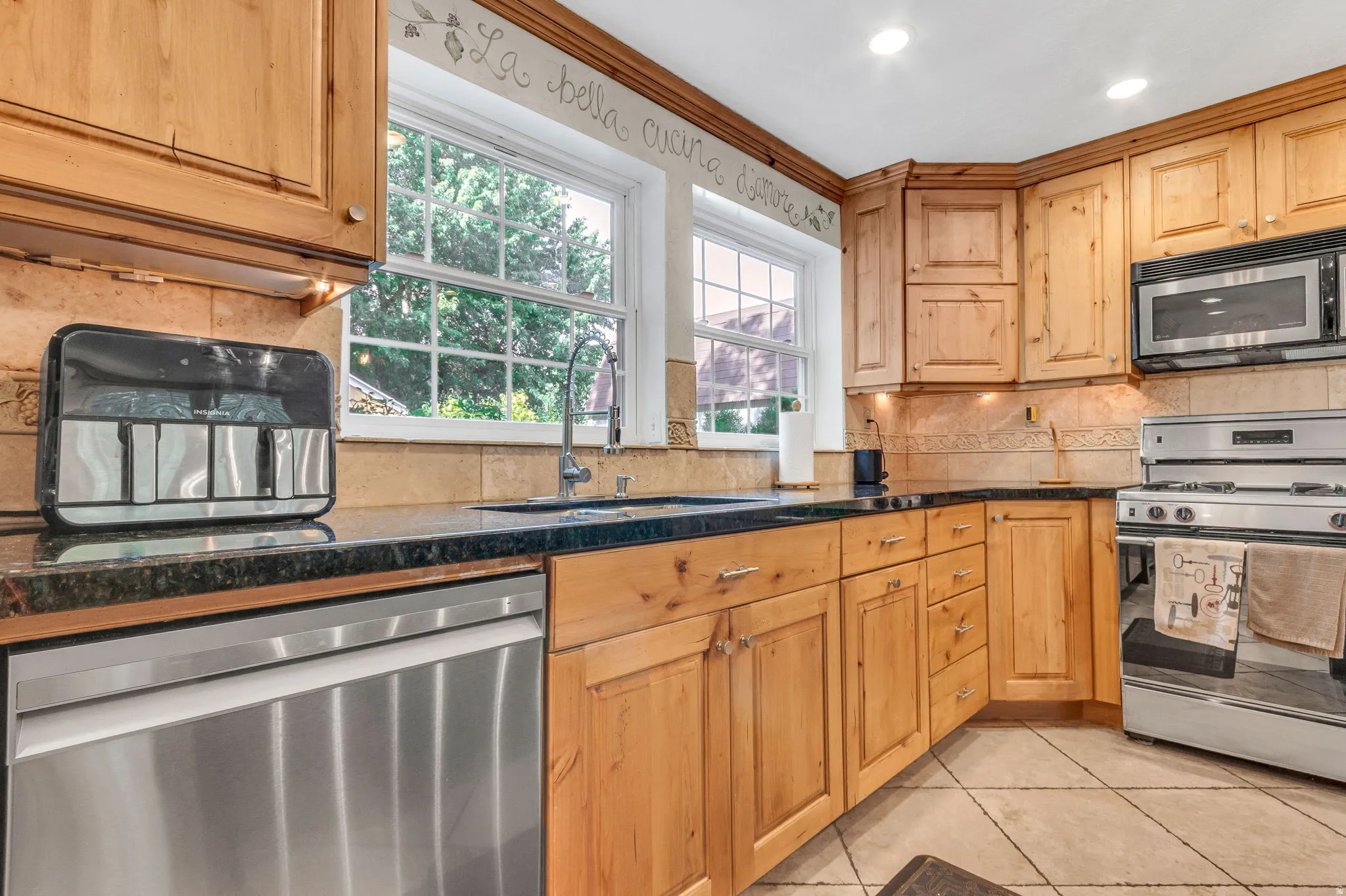 Kitchen featuring natural wood-finish cabinetry, dark countertops, a stainless steel dishwasher, and a stainless steel oven with an overhead microwave