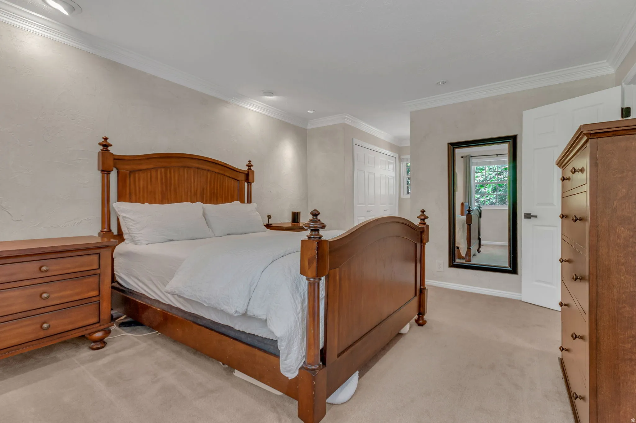 Master bedroom featuring textured wall finishes, crown molding, recessed lighting, and white bi-fold closet doors