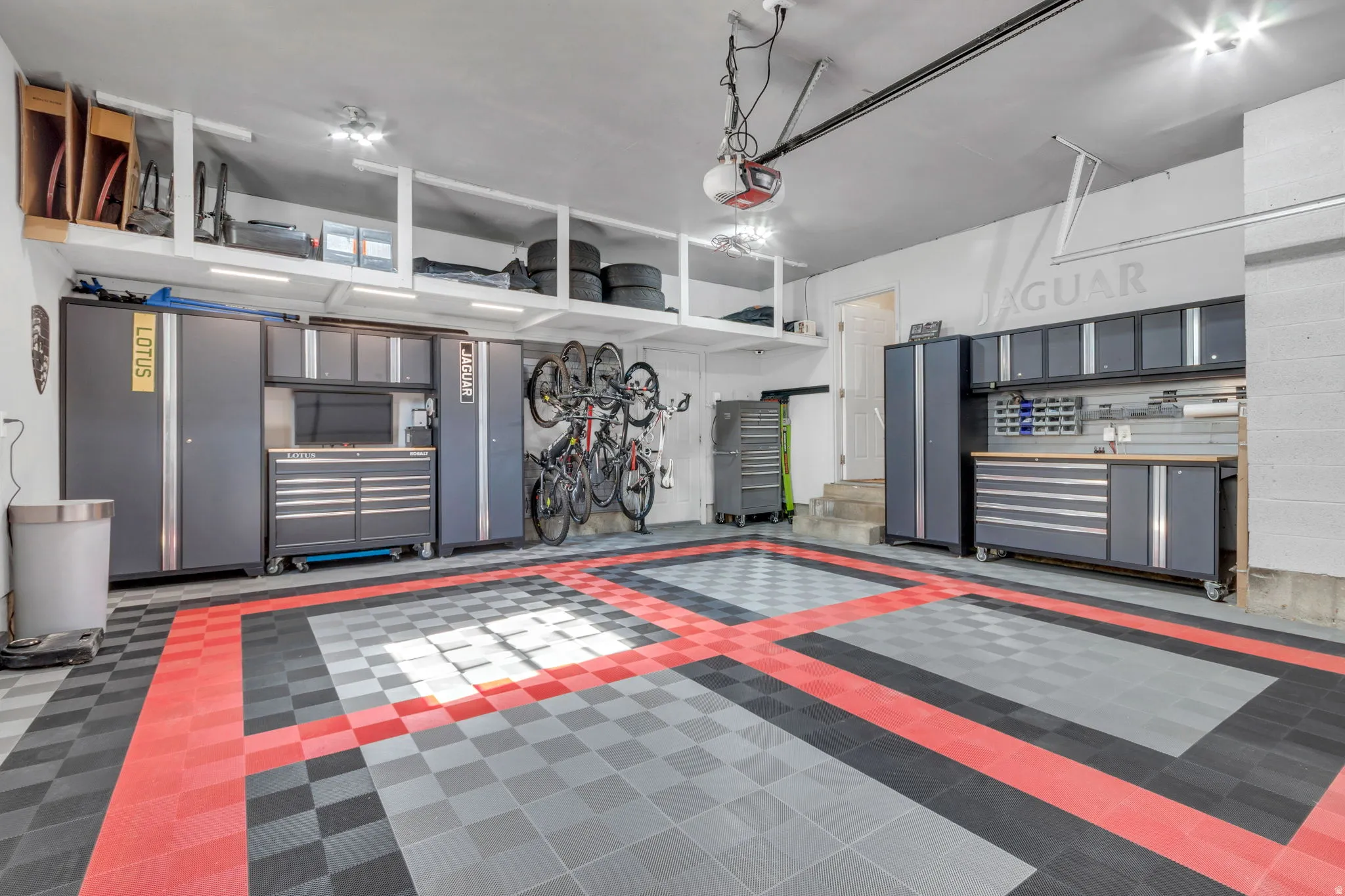 Spacious garage featuring a checkerboard floor pattern, extensive built-in storage cabinetry, overhead shelving, track lighting, and a built-in workbench area