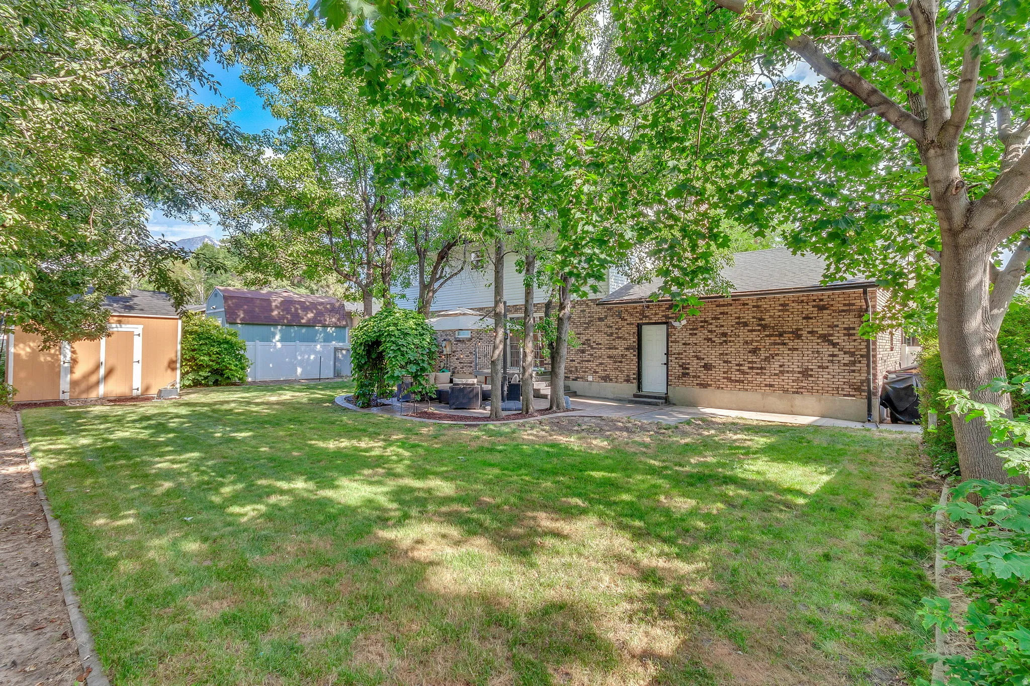 Expansive backyard featuring a manicured lawn, mature trees, and a brick-faced exterior