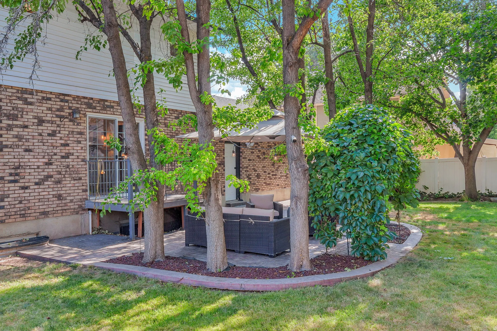 Expansive backyard featuring a manicured lawn, established trees, and a brick exterior