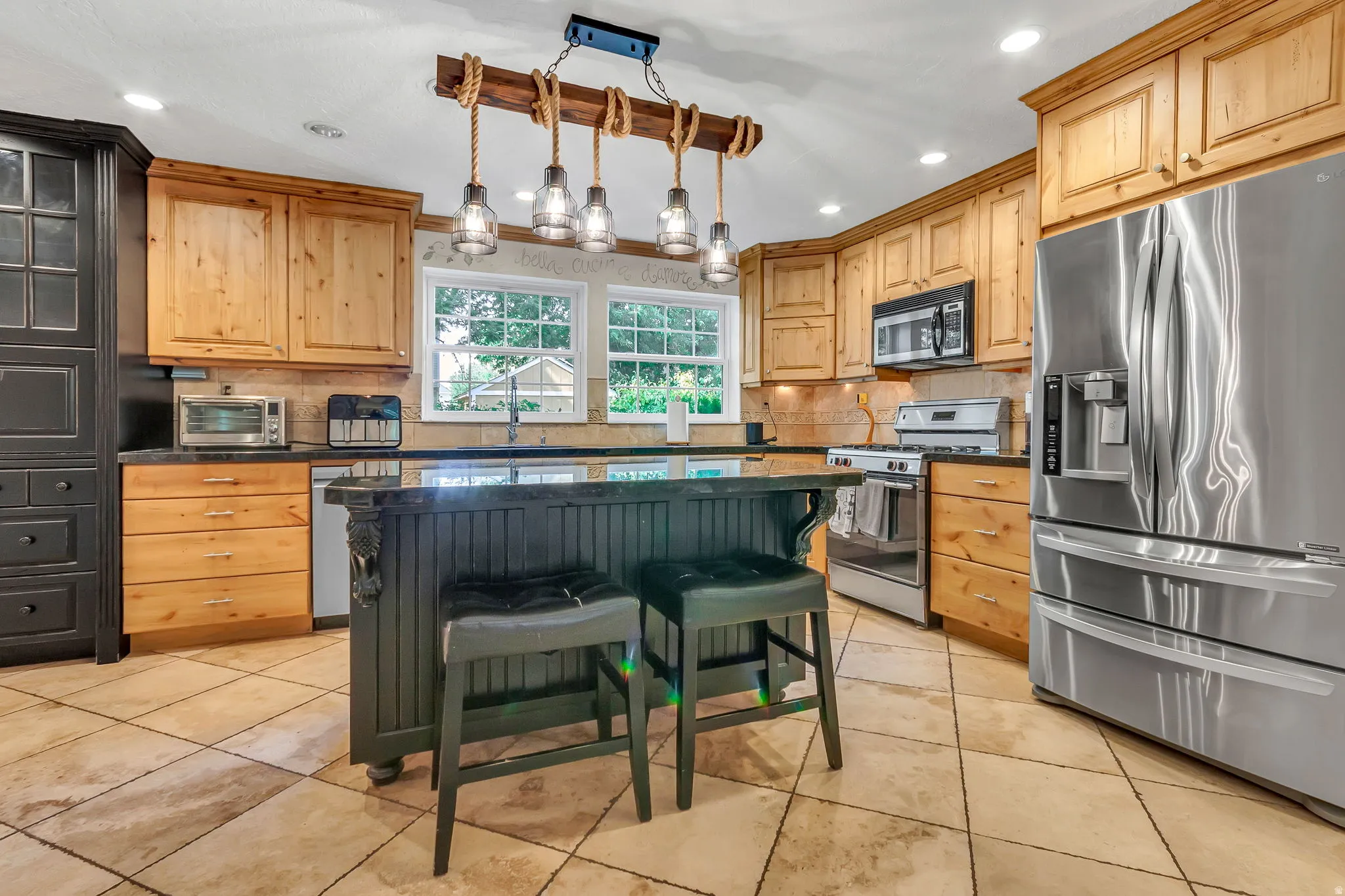 Kitchen featuring a central island with seating, natural wood cabinetry, stainless steel appliances, tiled flooring, and recessed lighting