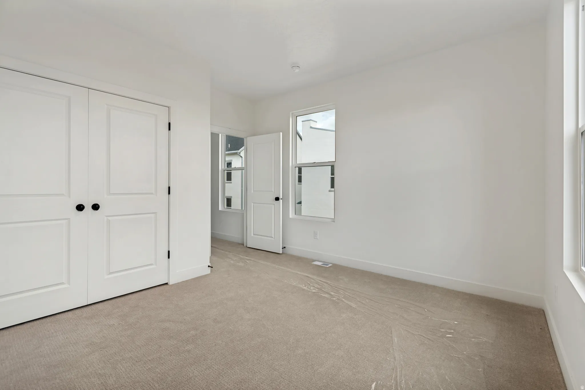 Neutral-toned carpeting, white walls, two-panel interior doors with matte black hardware, and multiple windows providing natural light