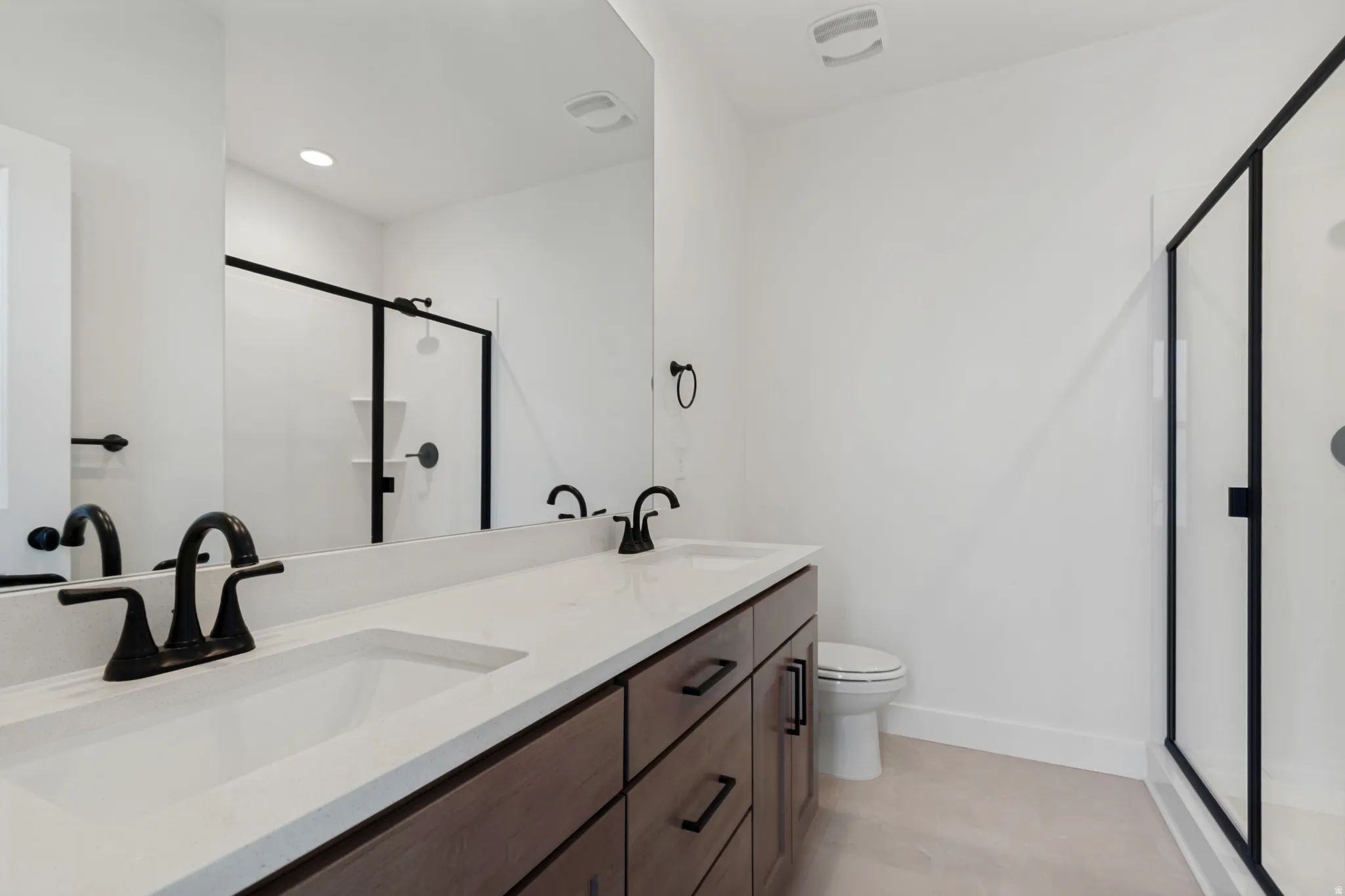 Dual vanity with integrated sinks, quartz countertop, dark wood-finish cabinetry with matte black hardware, and a glass-enclosed shower with matte black framing