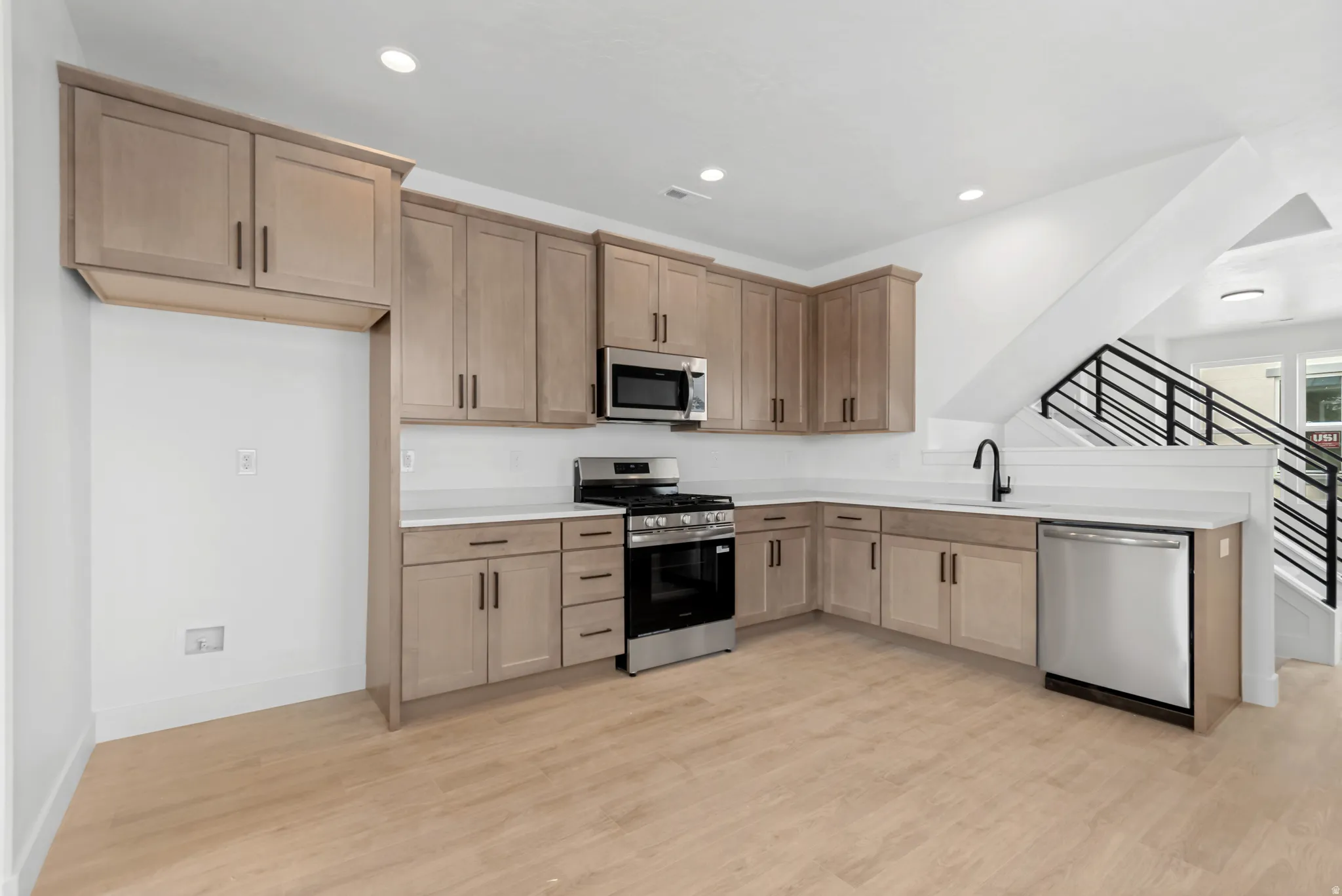 L-shaped kitchen with light wood-finish cabinetry, stainless steel appliances, white countertops, and wood-finish flooring