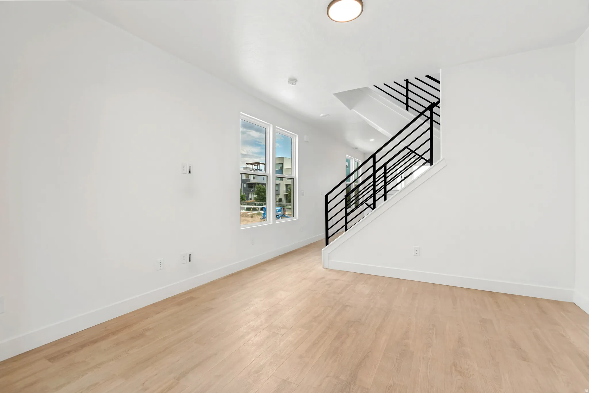 Light wood-finish flooring, white walls, large windows, and a modern staircase with black metal railing