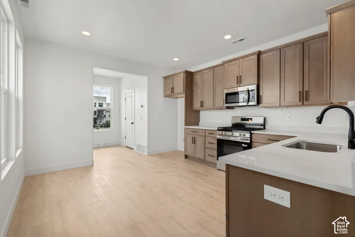 Kitchen featuring light wood-finish flooring, stainless steel appliances, solid surface countertops, and recessed lighting