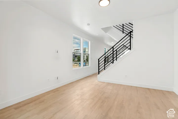 Light wood-finish flooring, white walls, large windows, and a modern staircase with black metal railing