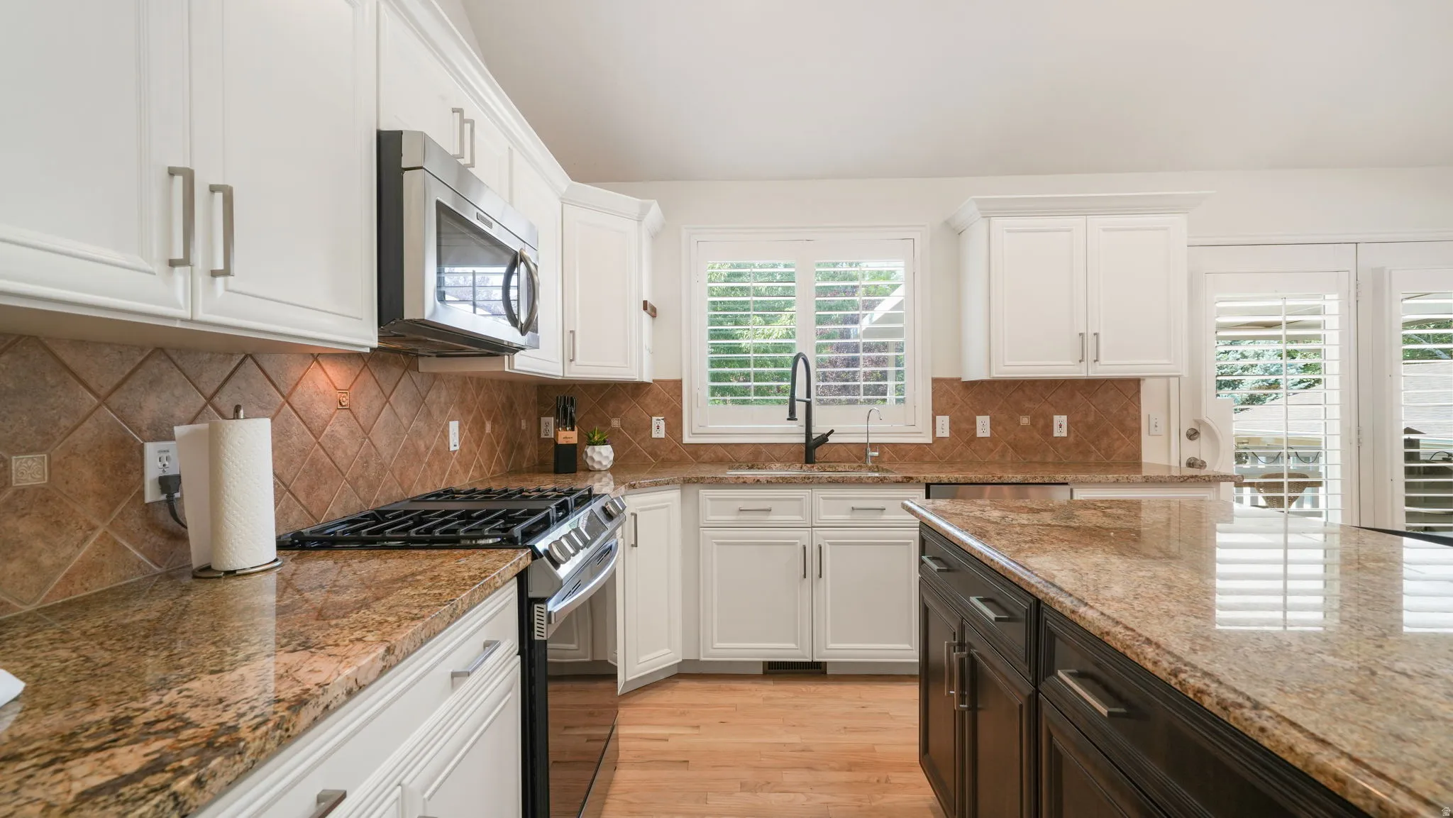 Kitchen featuring white cabinetry, granite countertops, a diamond-patterned tile backsplash, stainless steel appliances, and a central island with contrasting dark cabinetry