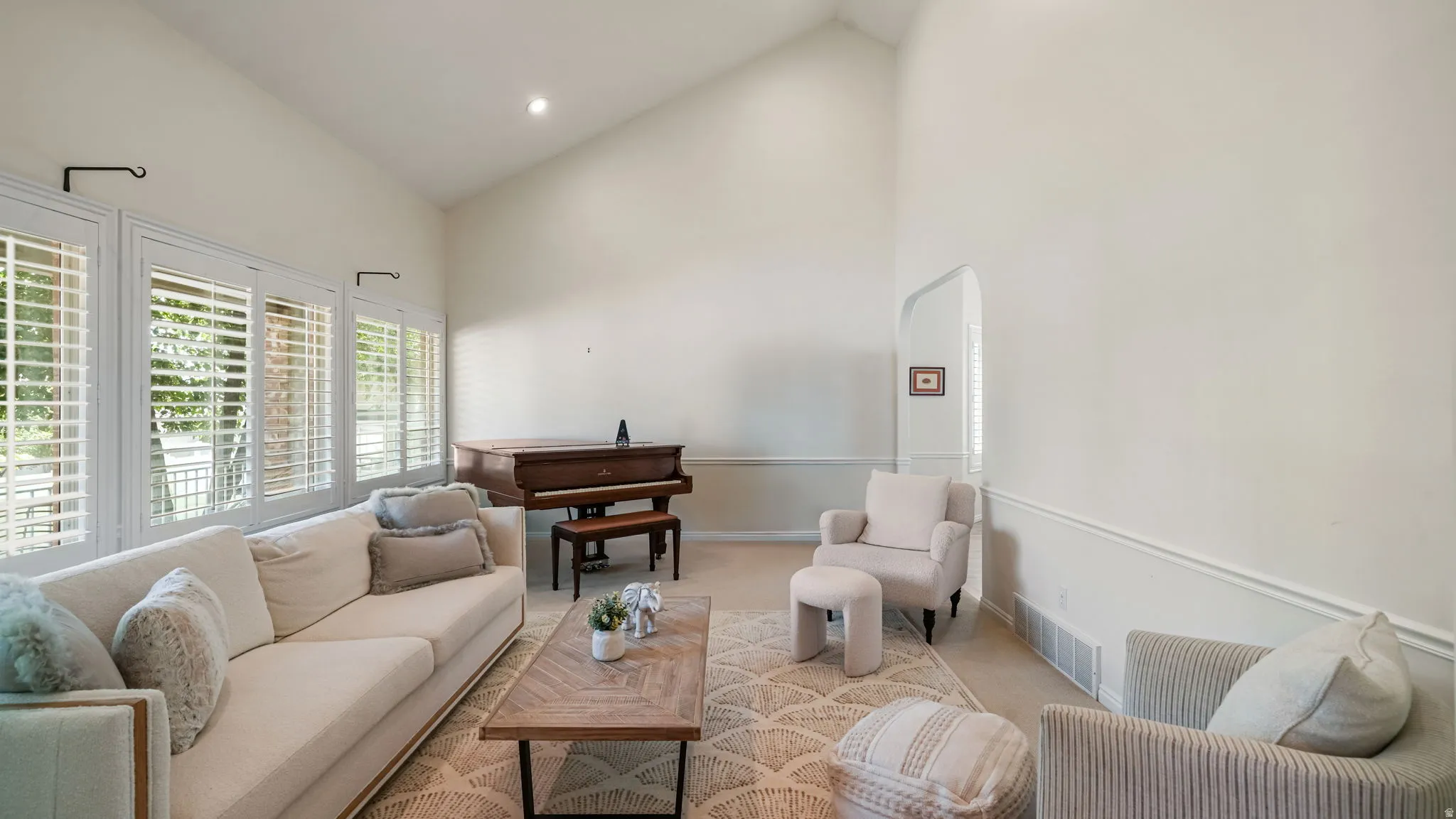 Living area featuring vaulted ceilings, a series of windows with plantation shutters, wainscoting, and recessed lighting