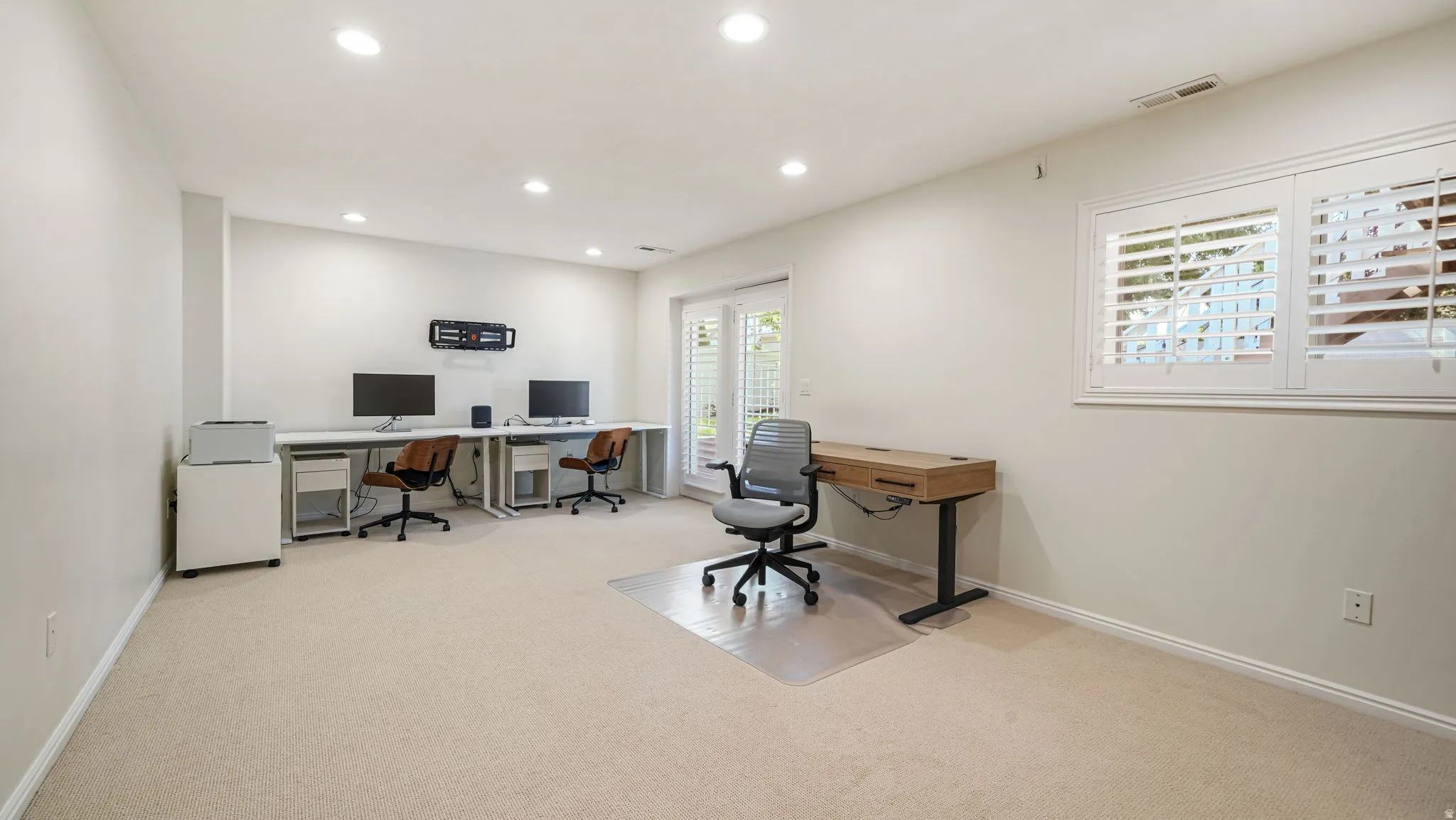 Spacious room featuring neutral carpeting, recessed lighting, and a window with white plantation shutters