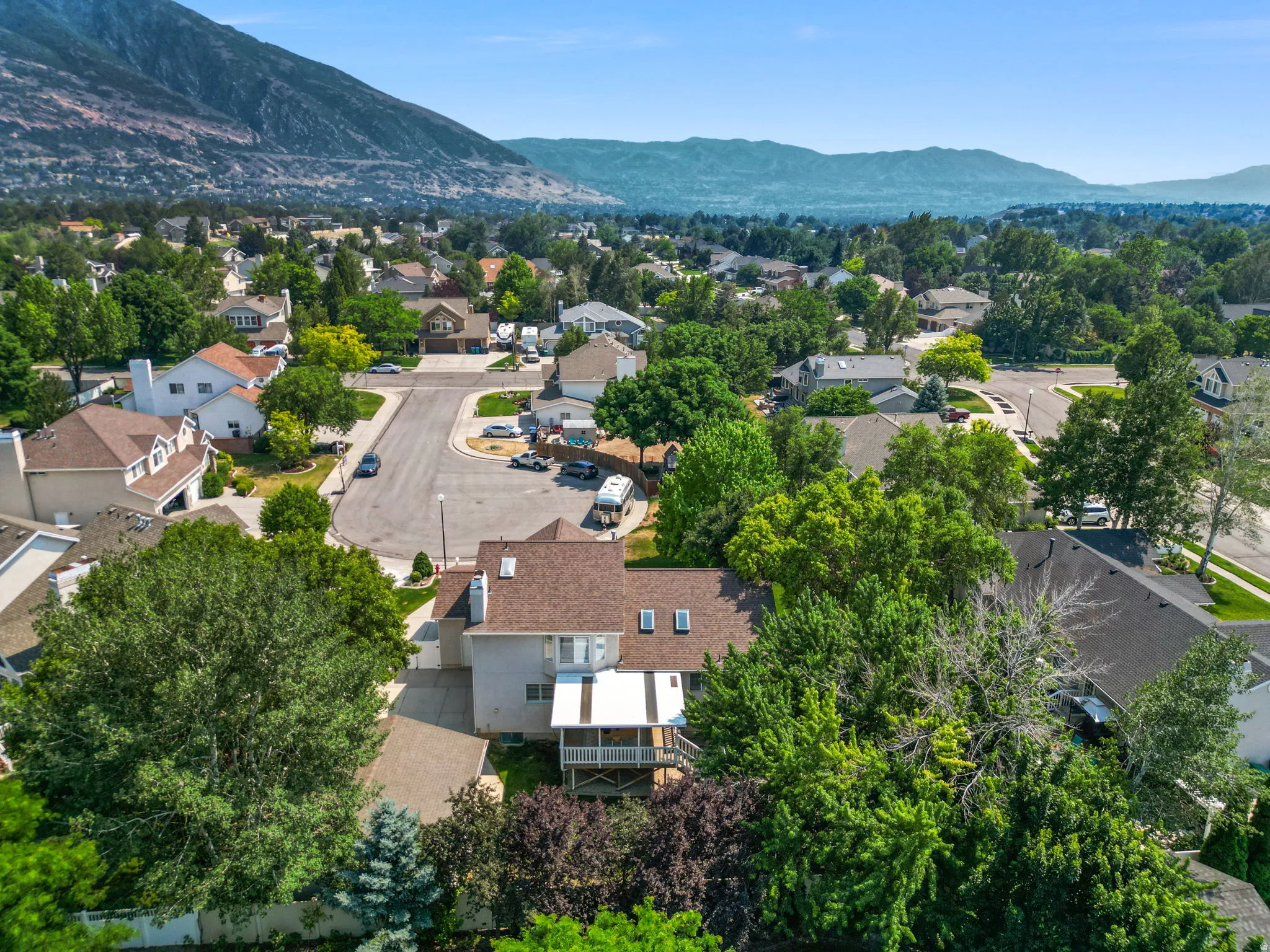 Aerial perspective showcasing a residential neighborhood with mature trees and mountain scenery