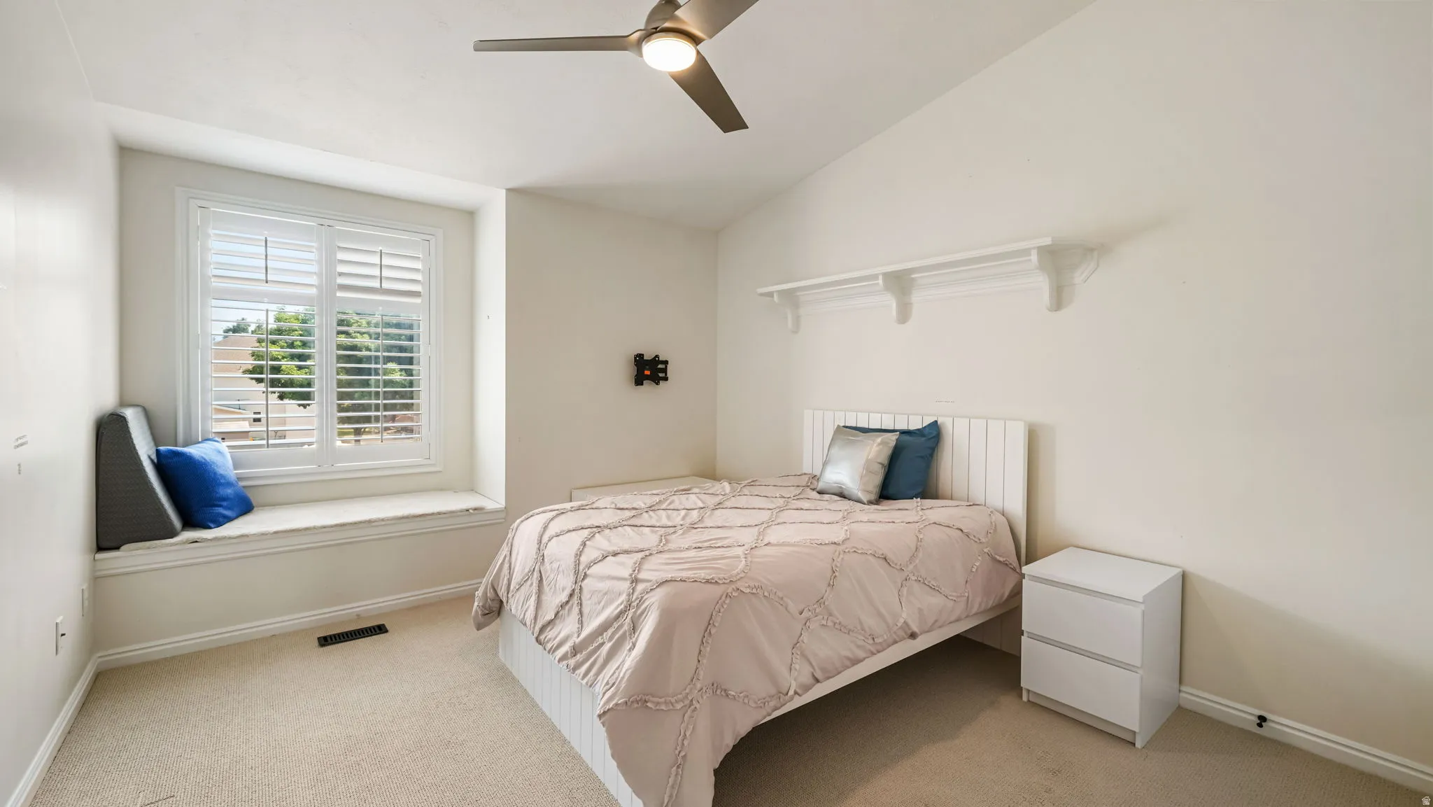 Window seat with plantation shutters, ceiling fan, carpeted flooring, and architectural wall shelving