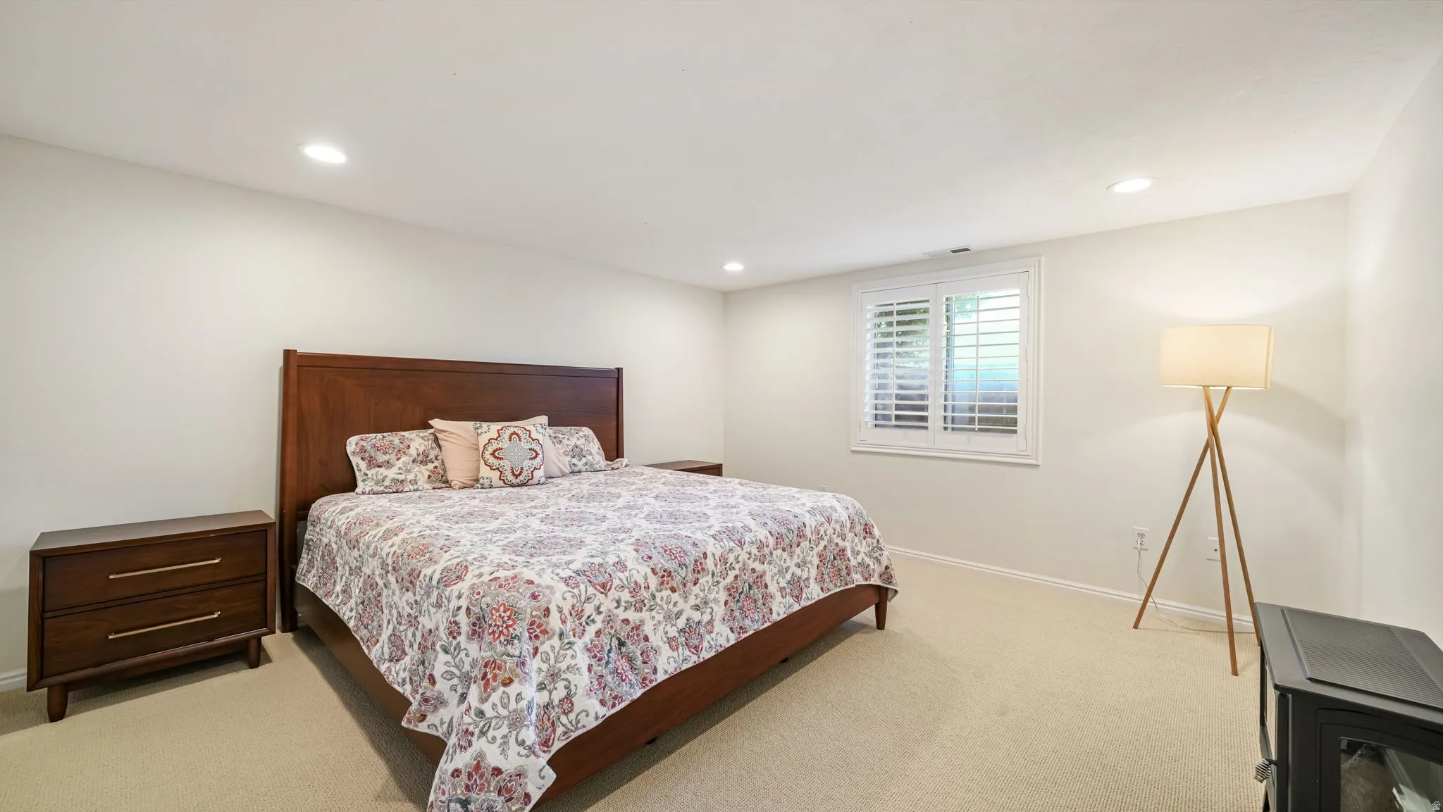 Spacious room featuring neutral carpet flooring, recessed ceiling lighting, and a window with white plantation shutters