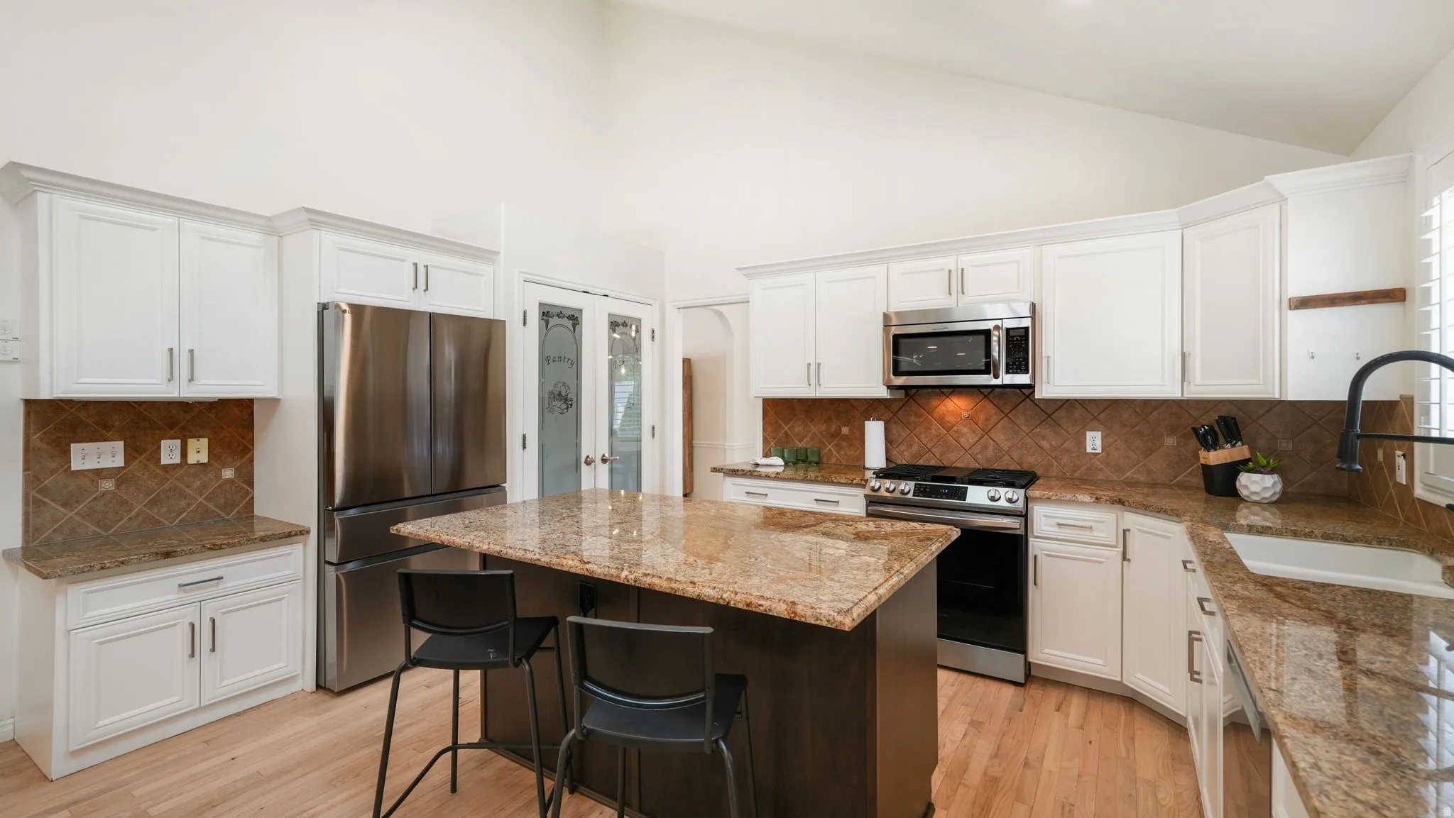 Kitchen featuring white cabinetry, stainless steel appliances, a central island with countertop seating, granite countertops, and a tiled backsplash