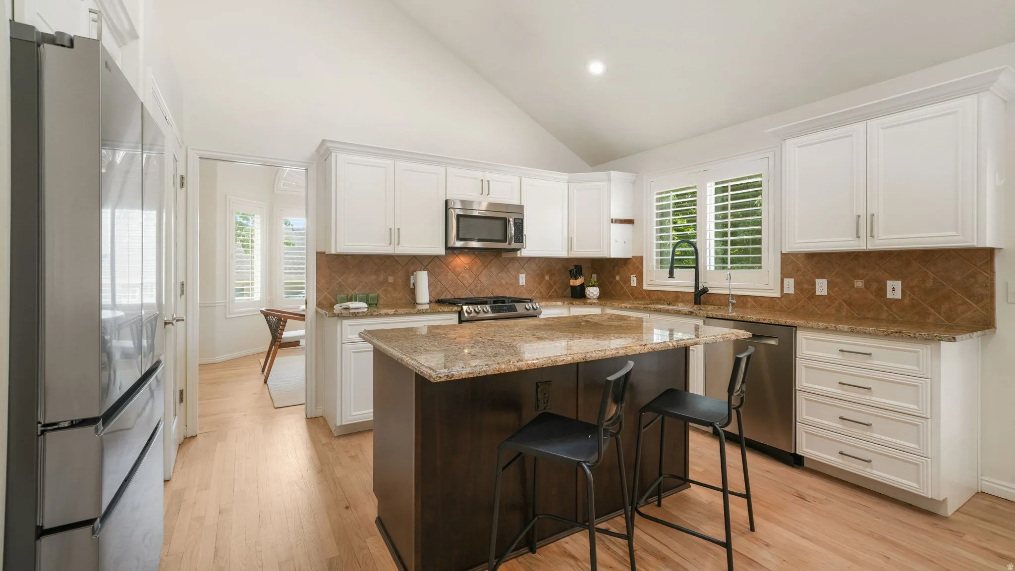 Kitchen featuring a central island with a granite countertop, white cabinetry with contemporary hardware, stainless steel appliances, a tile backsplash, and light wood-finish flooring