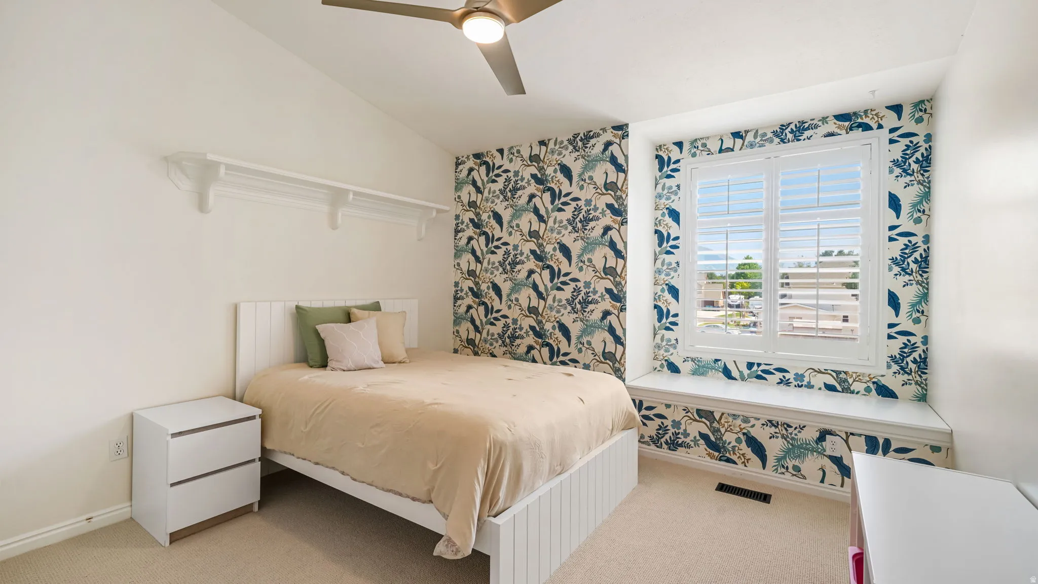 Vaulted ceiling room featuring a window seat, white plantation shutters, built-in shelving, a ceiling fan, and carpet flooring