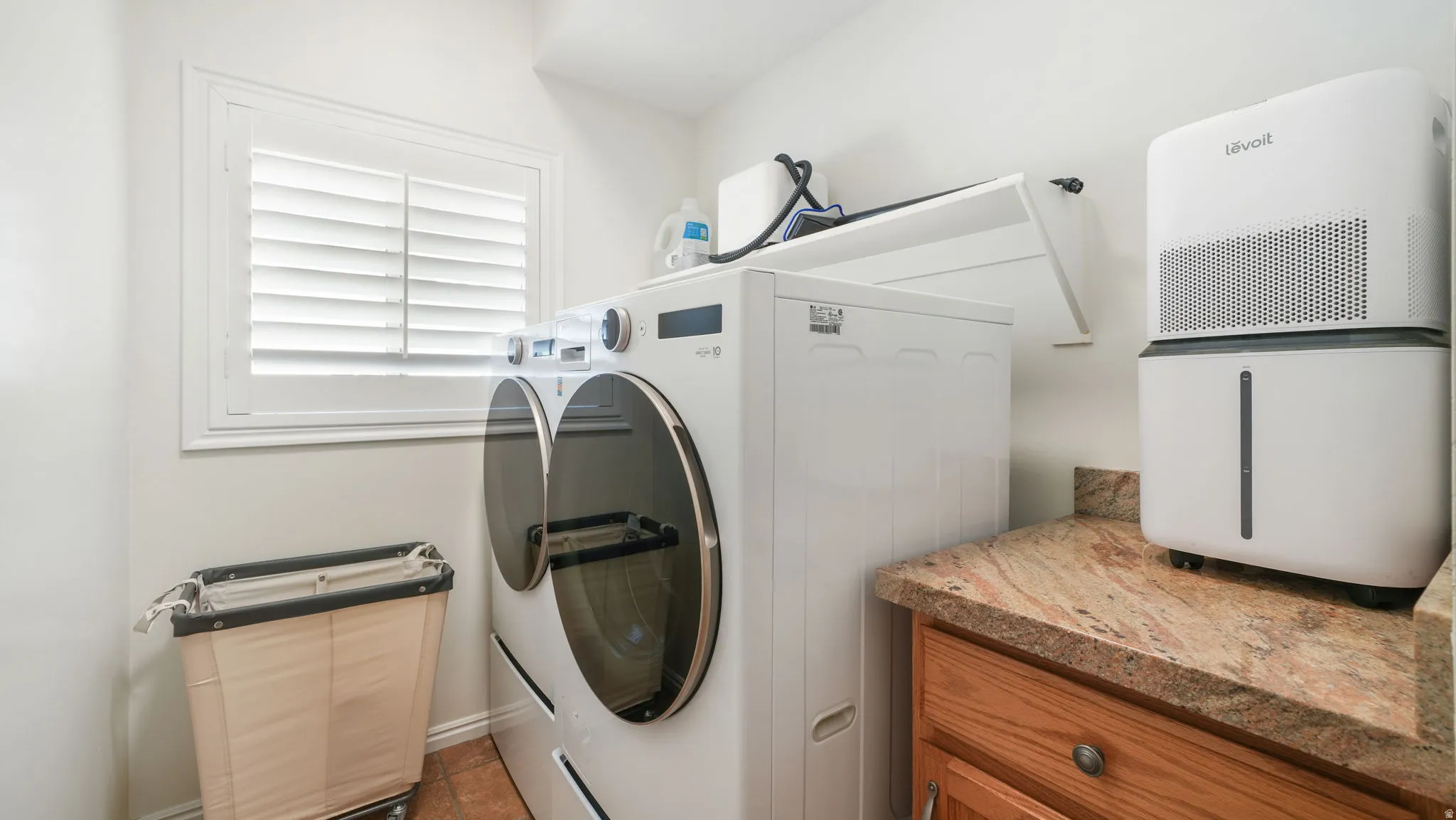 Functional laundry area featuring neutral wall tones, a window with plantation shutters, wood-finish flooring, a built-in countertop, and wood cabinetry