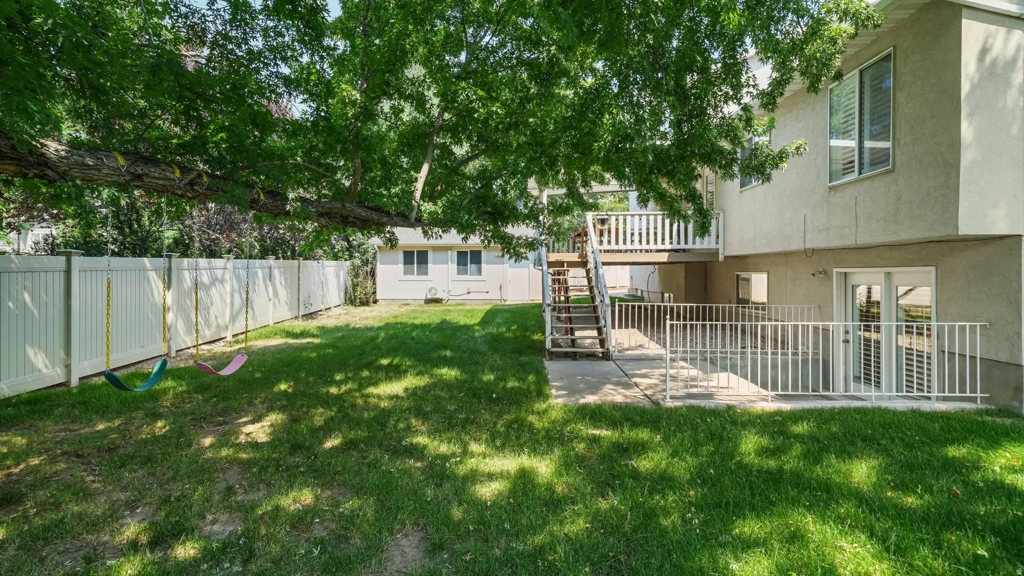 Expansive backyard featuring a green lawn, mature trees providing natural shade, and a white privacy fence