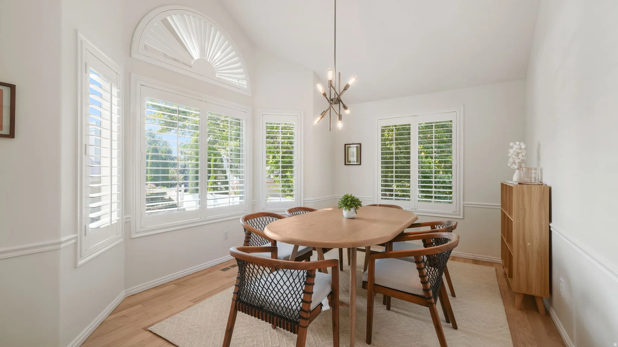 Dining space featuring multiple windows with plantation shutters, vaulted ceiling, and wood-finish flooring