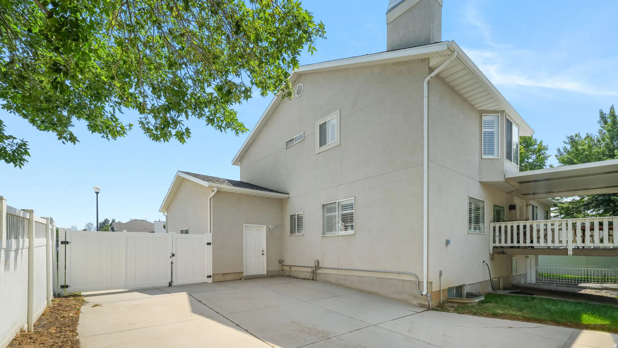 Stucco exterior with multiple windows, a concrete driveway, and a white vinyl fence