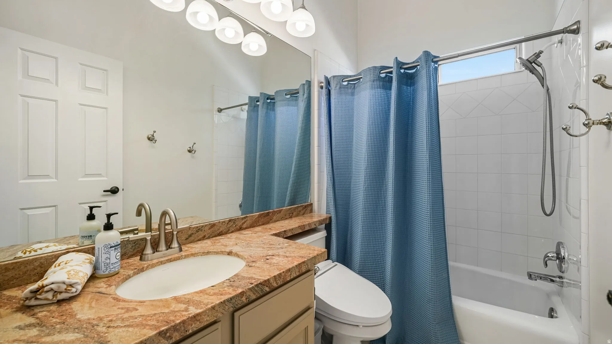 Bathroom featuring a vanity with an integrated sink and stone-finish countertop, a panel door, overhead lighting, a mirror, and a tub-shower combination with white tile surround