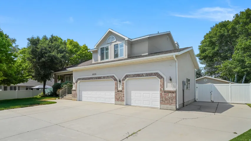 Exterior featuring a two-car garage with brick accents, an arched window dormer, and a wide concrete driveway