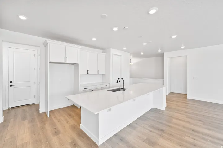 Spacious kitchen featuring a large island with an integrated sink and matte black faucet, surrounded by white cabinetry with black hardware