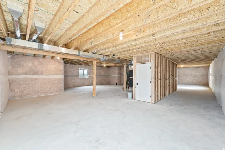Unfinished basement featuring exposed wood joists, concrete flooring, insulated walls, and a framed room with a white door