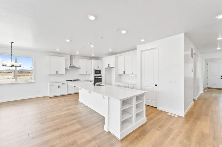 Open concept kitchen featuring an expansive central island with integrated shelving, recessed lighting, and light wood-finish flooring