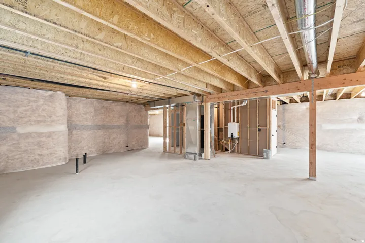 Unfinished basement space featuring exposed wood joists and subflooring, concrete slab flooring, insulated walls, and visible plumbing rough-ins
